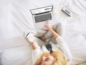Photo d'une femme entrain de travailler sur son ordinateur assise sur un lit